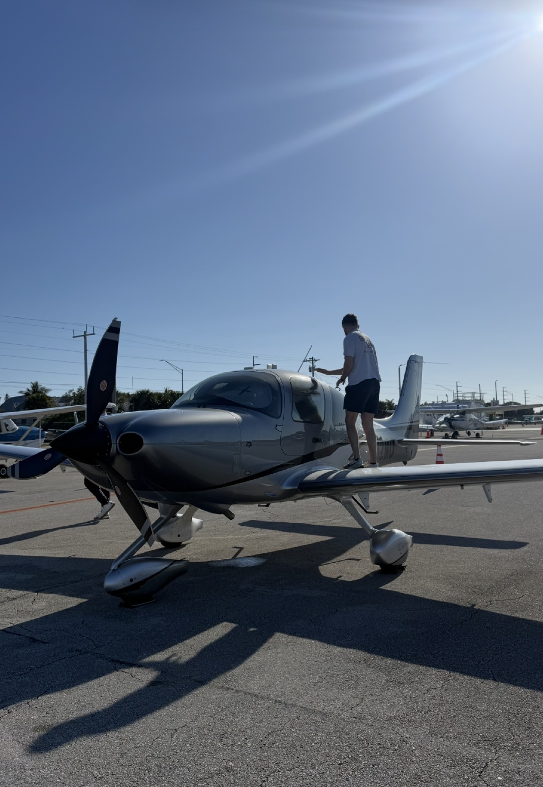 Dawson Gant standing on the wing of a silver airplane at a sunny airfield during pre-flight checks
