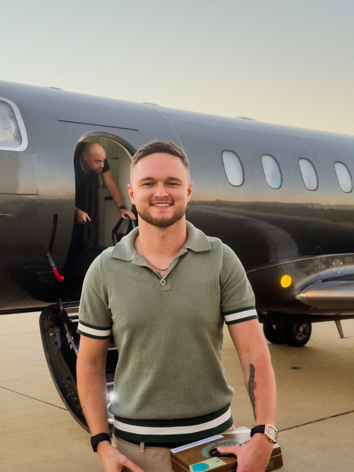 Dawson Gant smiling on the tarmac beside a private jet at golden hour